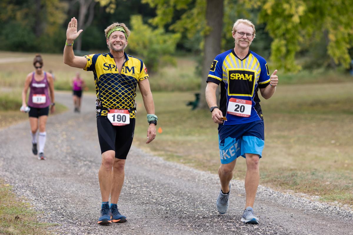 Two men in shirts advertising Spam walking towards the camera during a race.